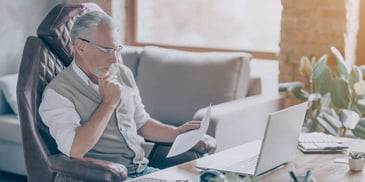 man reviewing his finances on a computer and paper statements