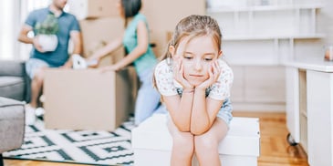 Child sits on top of a box while her parents pack up after their divorce