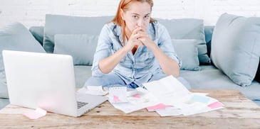 Woman looks at a pile of bills in front of her computer