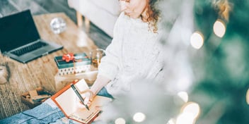 woman sitting by holiday tree and presents as she writes in her journal