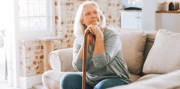 thoughtful woman with cane on couch