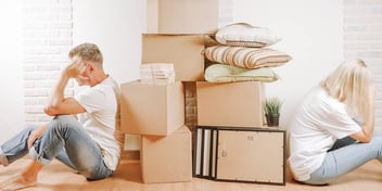 divorcing couple sitting apart with stacks of boxes and clutter