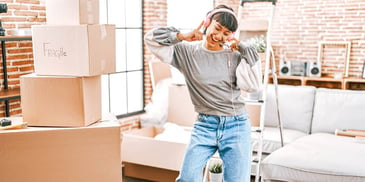 woman happily listening to music as she unpacks moving boxes in her new loft