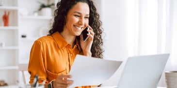 woman holding paperwork and smiling as she talks on the phone