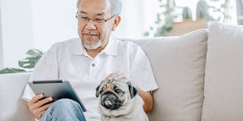 man sitting on the couch with his pug dog reading on his tablet