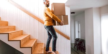man carrying moving boxes down the stairs of his home