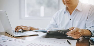man looking at laptop and notebook on desk