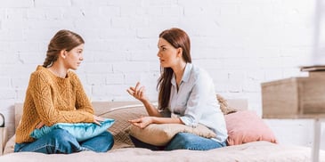 mother and daughter sitting on a bed having a conversation