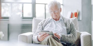 older gentleman sitting in a chair and reading on his tablet