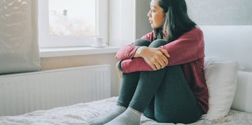 sad woman sitting alone on her bed looking out the window