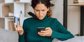 stressed out woman looking at her phone with credit card in hand