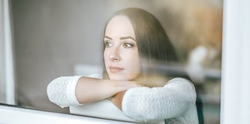 woman looking out a window with a pensive look on her face