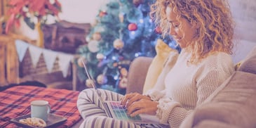 woman sitting by her christmas tree with cocoa and cookies working on her computer