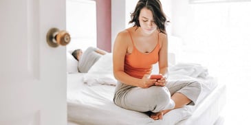woman texting someone else while her husband sleeps in bed next to her