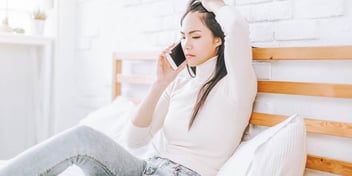 distressed woman sitting on bed talks on the phone
