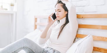 distressed woman sitting on bed talks on the phone