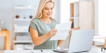 Young blond woman examining document with laptop open