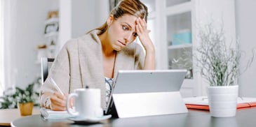 Young woman on her computer looking distraught and writing on a notepad
